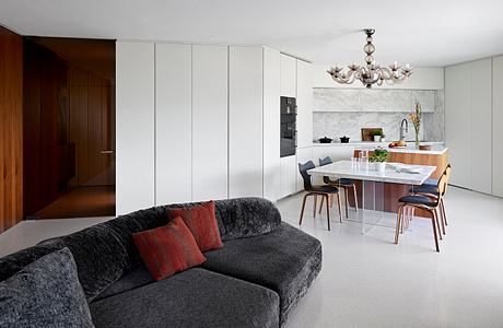 A modern, open-concept kitchen and living space with sleek cabinetry, marble countertops, and a chandelier.