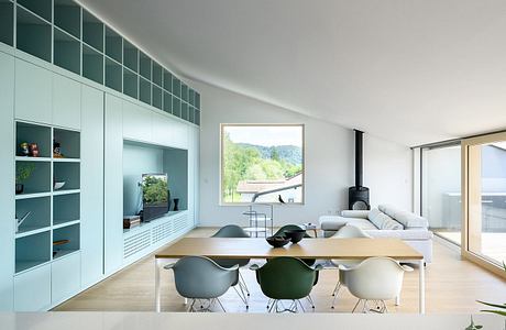 Minimalist living room with wooden dining table, green chairs, and large window overlooking nature.