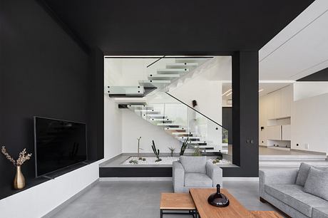 Striking minimalist interior with glass-enclosed staircase, sleek gray furnishings, and nature-inspired accents.
