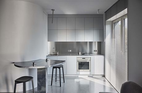 Minimalist kitchen with sleek gray cabinetry, stainless steel appliances, and a curved breakfast bar.