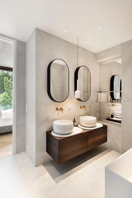A modern bathroom with minimalist dark oval mirrors, wooden vanity, and white vessel sinks.