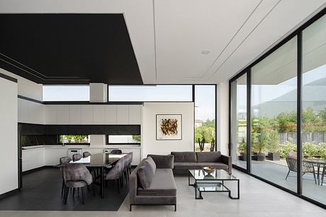 Modern open-plan kitchen and living room with sleek black and white decor, large windows.
