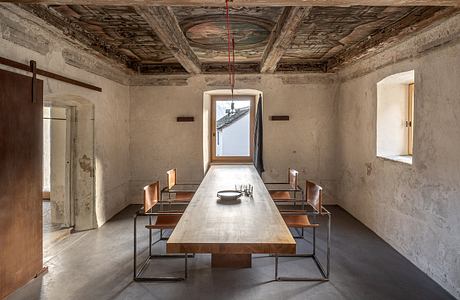 Rustic dining room with ornate wooden ceiling, large table, and minimalist bench seating.