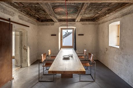 Rustic dining room with ornate wooden ceiling, large table, and minimalist bench seating.