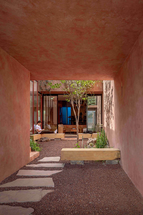 A warm, earthy-toned interior courtyard with a central tree and wooden seating.