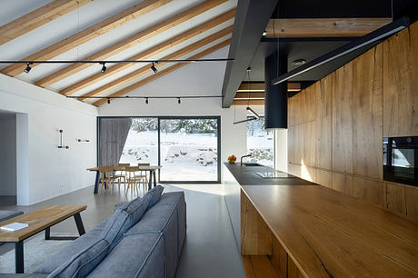 Spacious, modern cabin-style interior with exposed wooden beams, sleek kitchen, and large windows.