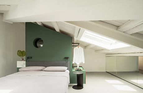 Minimalist and airy bedroom with green accent wall, slanted ceiling, and bright skylight.