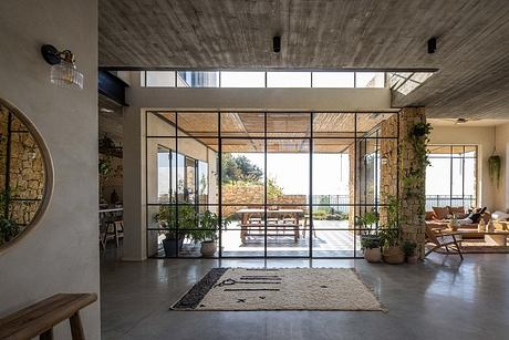 Minimalist concrete interior with large panoramic windows overlooking lush outdoor scenery.