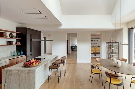 An open-concept modern kitchen and dining area with sleek cabinetry, natural wood flooring, and a marble island.