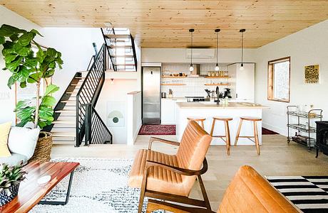 Cozy open-concept kitchen with wooden beams, metal stairs, and patterned rugs.