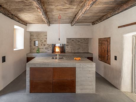 A rustic kitchen with exposed wooden beams, concrete countertops, and a wood-burning stove.