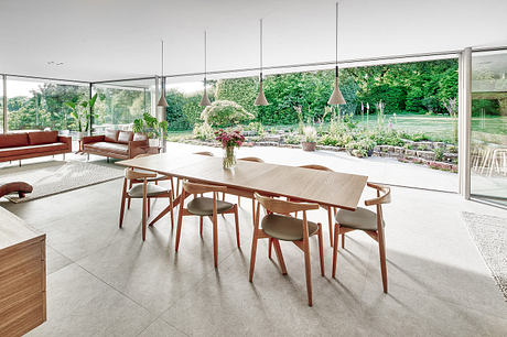 Airy open-plan dining area with wood furniture, modern pendant lights, and panoramic garden views.