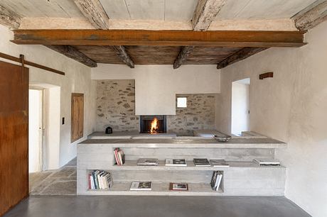 Rustic stone fireplace with wooden ceiling beams and built-in concrete shelves.