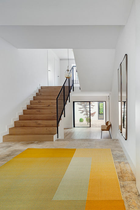 Elegant wooden stairs, sleek metal railing, and vibrant yellow rug in modern foyer.