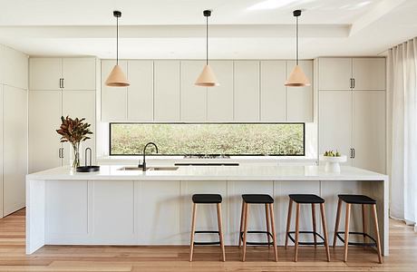 Modern, minimalist kitchen with sleek white cabinetry, pendant lighting, and a panoramic window overlooking greenery.