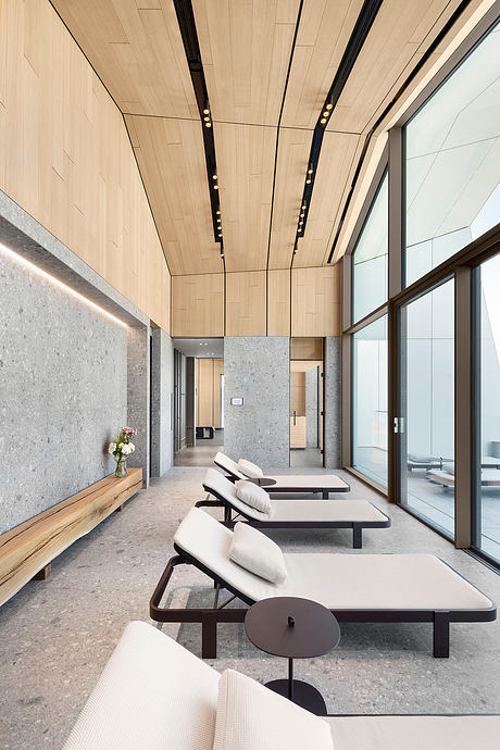 Modern interior with wooden paneled ceiling, gray stone walls, and sleek lounge chairs.