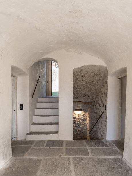 A cozy, stone-walled interior with an arched doorway, a wooden door, and a stone staircase.