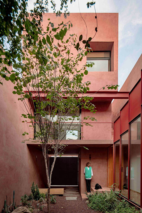A striking modern building with vibrant pink walls, cascading greenery, and a person visible through the entryway.