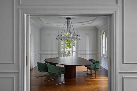 Elegant dining room with ornate moldings, chandelier, and green upholstered chairs.