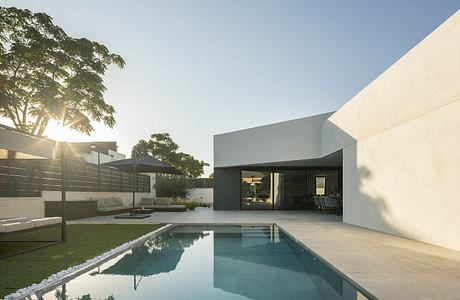 A modern, minimalist home with a pool reflecting the surrounding trees and sky.