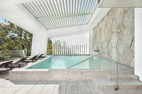 Elegant modern pool area with sleek white ceiling beams, stone walls, and lounge chairs.