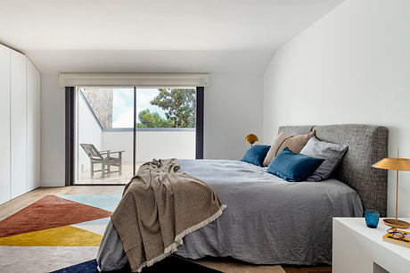 Minimalist bedroom with large sliding glass door, geometric rug, and neutral-toned furniture.