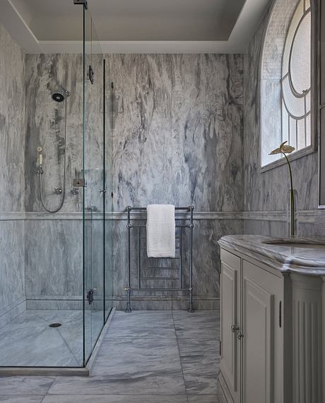 A sophisticated bathroom design with marble-patterned walls, glass shower, and towel rack.