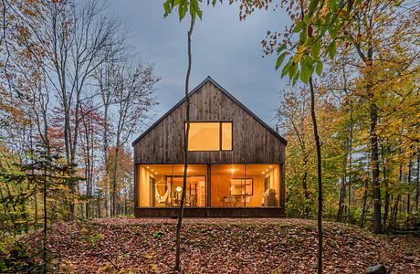 A cozy wooden cabin nestled in an autumn forest, illuminated by warm interior lighting.