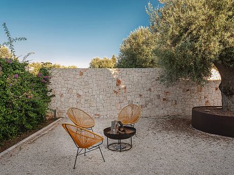 Intimate outdoor seating area with stone wall, wicker chairs, and a fire pit.