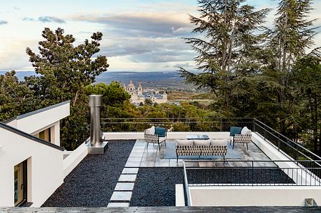 Modern patio with sleek furniture overlooking picturesque town and mountains.