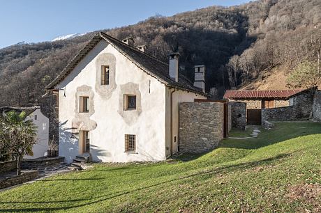 A rustic mountain cottage with stone walls, tiled roof, and grassy surroundings.
