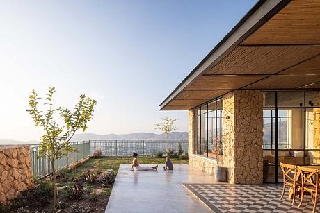 Outdoor patio with stone walls, wooden roofing, and mountain view. Checkerboard floor pattern.