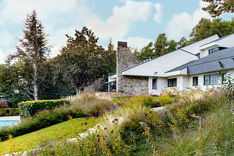 A contemporary home with a stone chimney, surrounded by lush landscaping and a swimming pool.