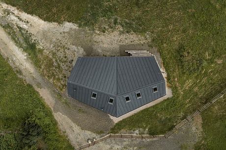 Aerial view of a modern, angular building with a pitched gray metal roof and windows.