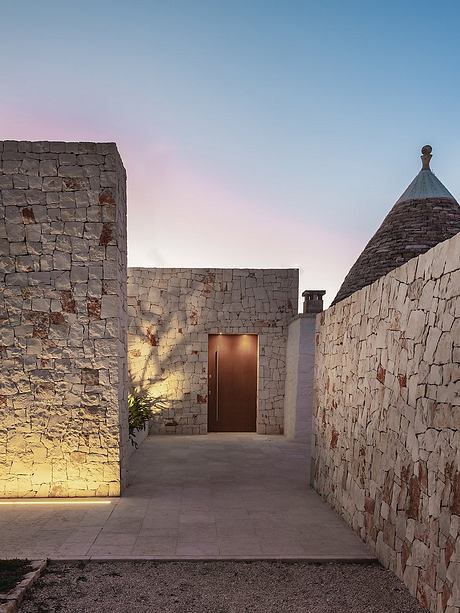 Striking exterior of a stone building with a domed roof and a wooden door, set against a colorful sky.