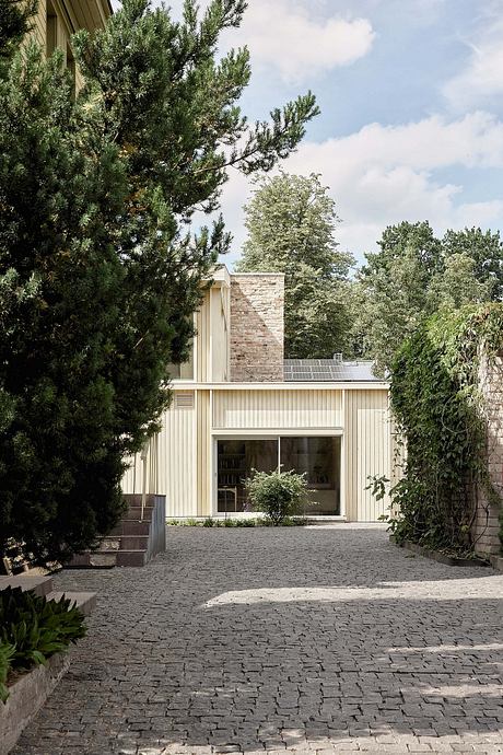 A modernist-inspired home with a stone chimney, wood siding, and a cobblestone driveway.