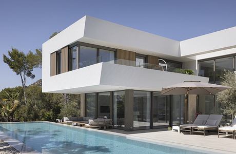 A modern, sleek villa with minimalist architecture, large glass windows, and a pool.