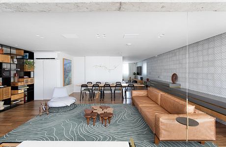 A modern open-plan living space with light wooden floors, minimalist furniture, and a graphic area rug.