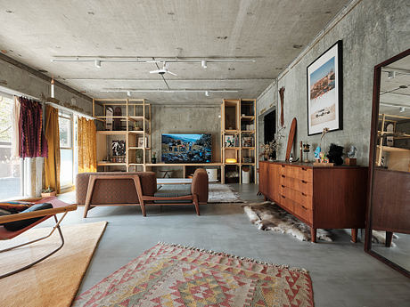 Mid-century modern living room with concrete walls, wood furniture, and abstract rug.