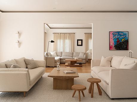 Spacious, minimalist living room with neutral tones, wooden accents, and a vibrant artwork.