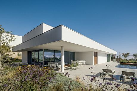 Modern, minimalist home with sleek white exterior, large windows, and outdoor patio with pool.