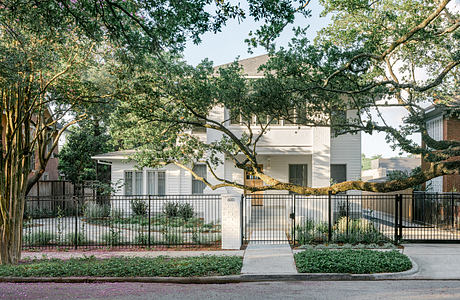 Stately white home framed by lush trees and decorative metal fence, exuding classic Southern charm.