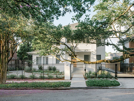 Stately white home framed by lush trees and decorative metal fence, exuding classic Southern charm.