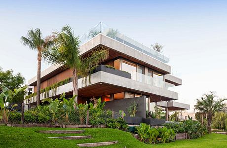 A modern, multi-level building with concrete and wood accents, surrounded by lush greenery.