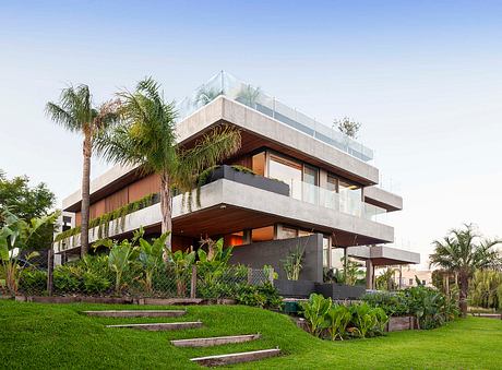 A modern, multi-level building with concrete and wood accents, surrounded by lush greenery.