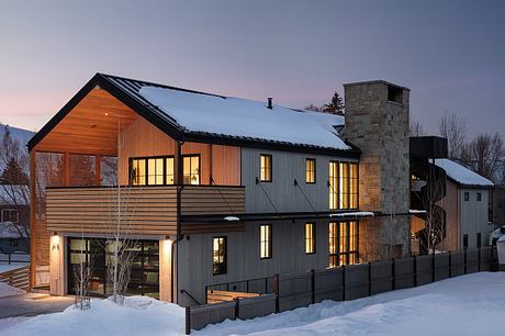 A modern, multi-story cabin with a stone chimney, wooden exterior, and large windows.