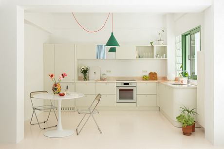 Modern, minimalist kitchen with sleek white cabinets, green pendant light, and simple furnishings.