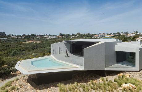 Modern, minimalist villa with geometric forms, glass walls, and a swimming pool overlooking a lush landscape.