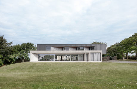 Modern, minimalist architecture featuring sleek lines, large windows, and a grassy lawn.