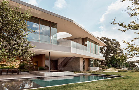 Modern glass and brick house with pool, surrounded by lush greenery.